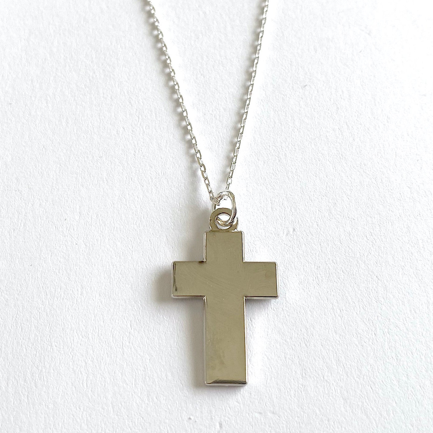A charm in the shape of a cross with a silver-tone steel chain against a white background.