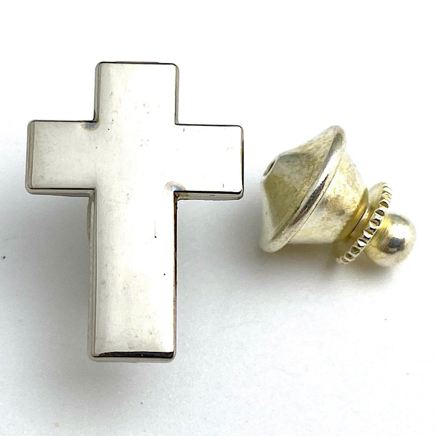 A silver-colored metal cross lapel pin with a gold-colored metal clasp.