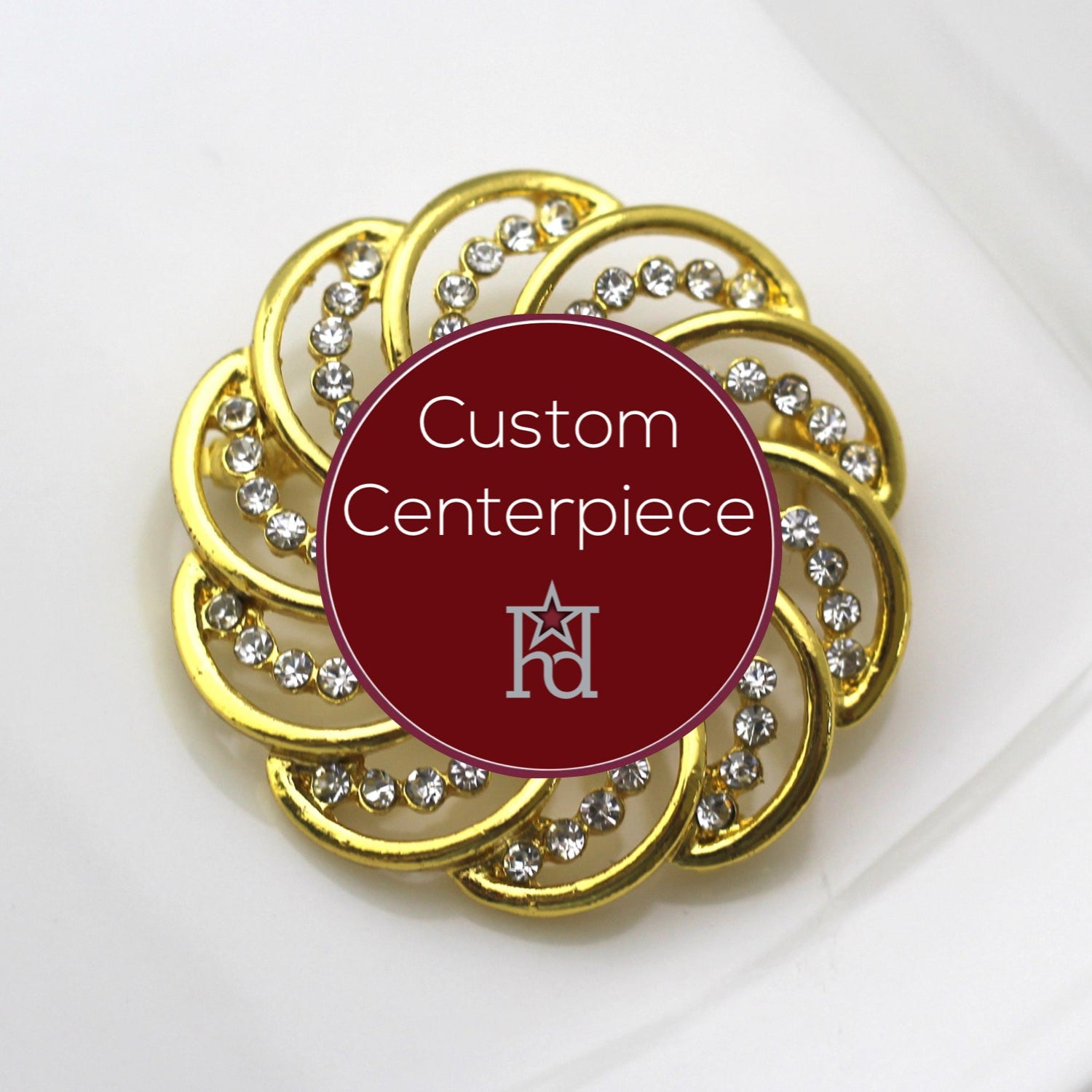 A gold-colored brooch with clear crystals designed in a circular pattern with a custom centerpiece.