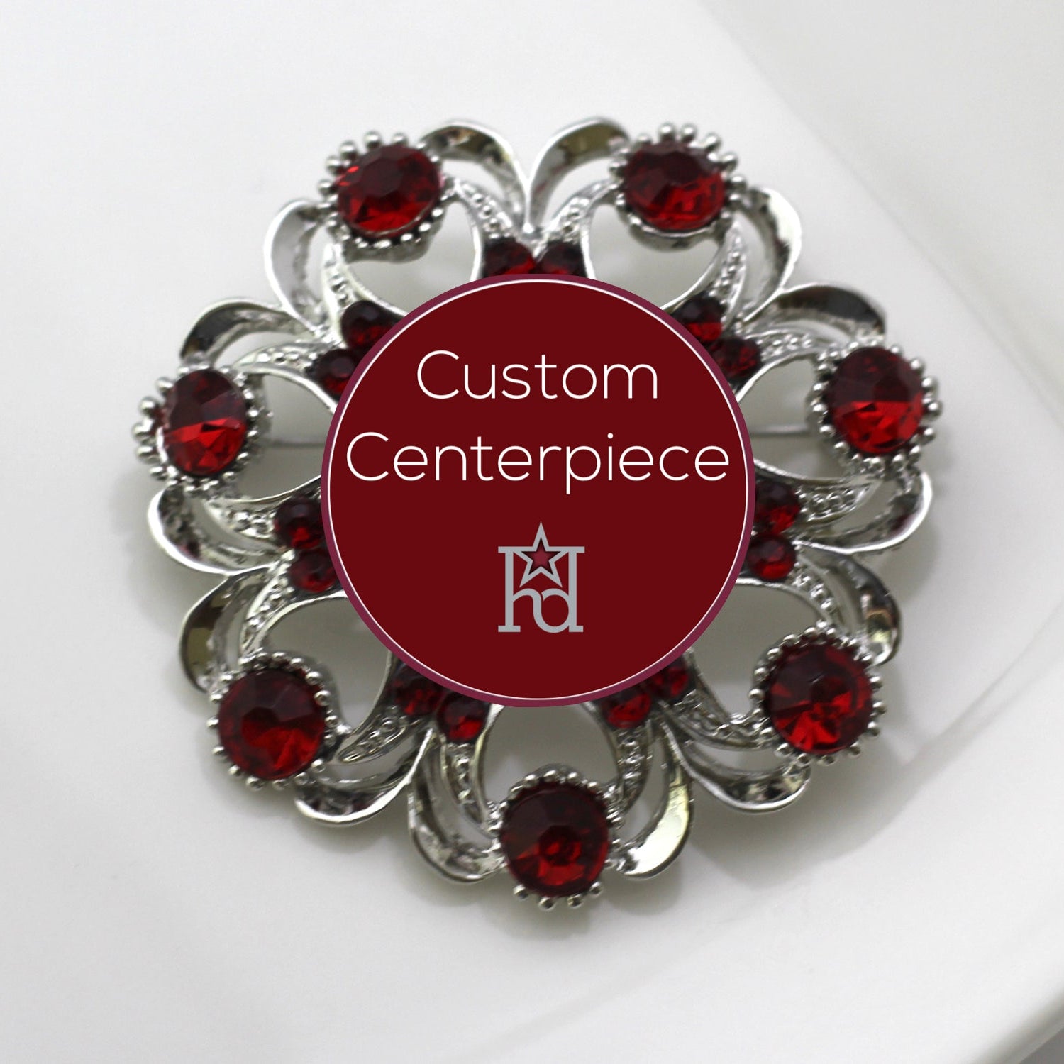 A round silver brooch with red crystals arranged in a pattern around a custom centerpiece.