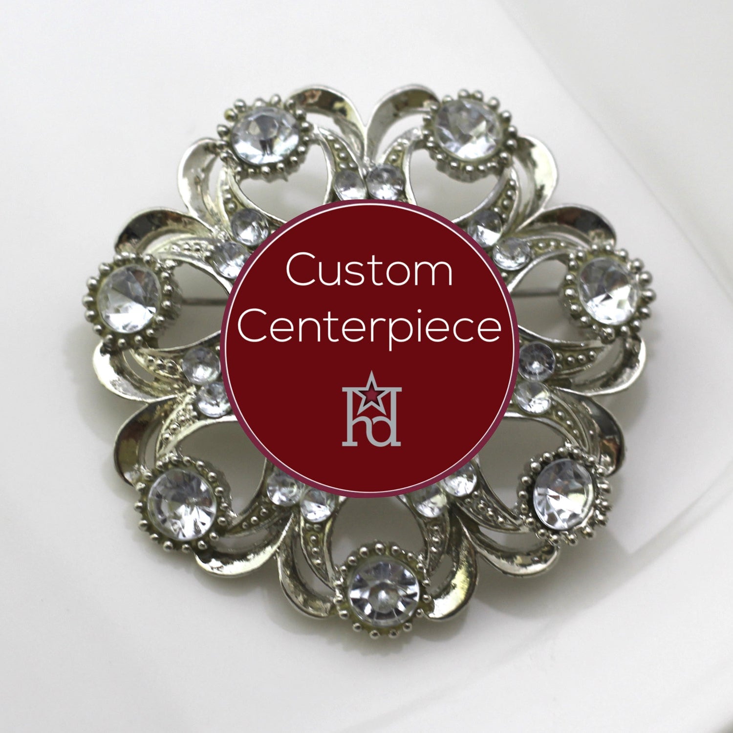 A round silver brooch adorned with clear crystals and a custom centerpiece with the initials 'RJ'.