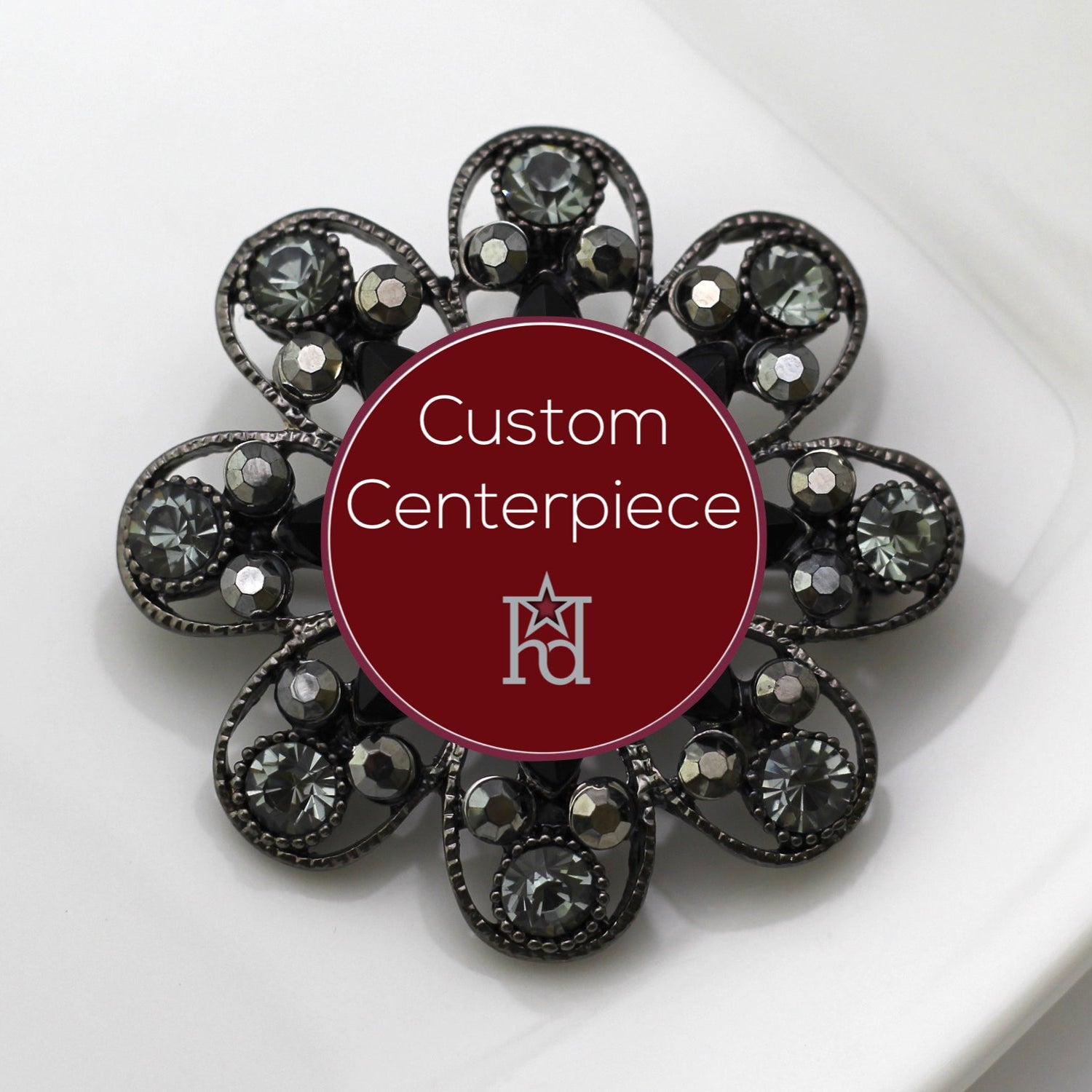 A silver brooch with black and grey crystals, featuring a circular design with a central label stating 'Custom Centerpiece' and the Hope Design logo.