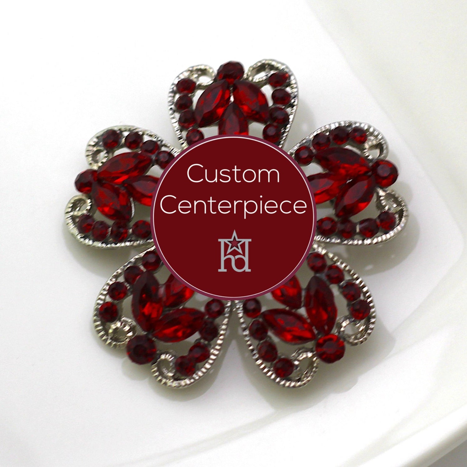A silver brooch with red crystals designed as a flower, featuring a custom centerpiece with the logo of Hope Design Ltd.