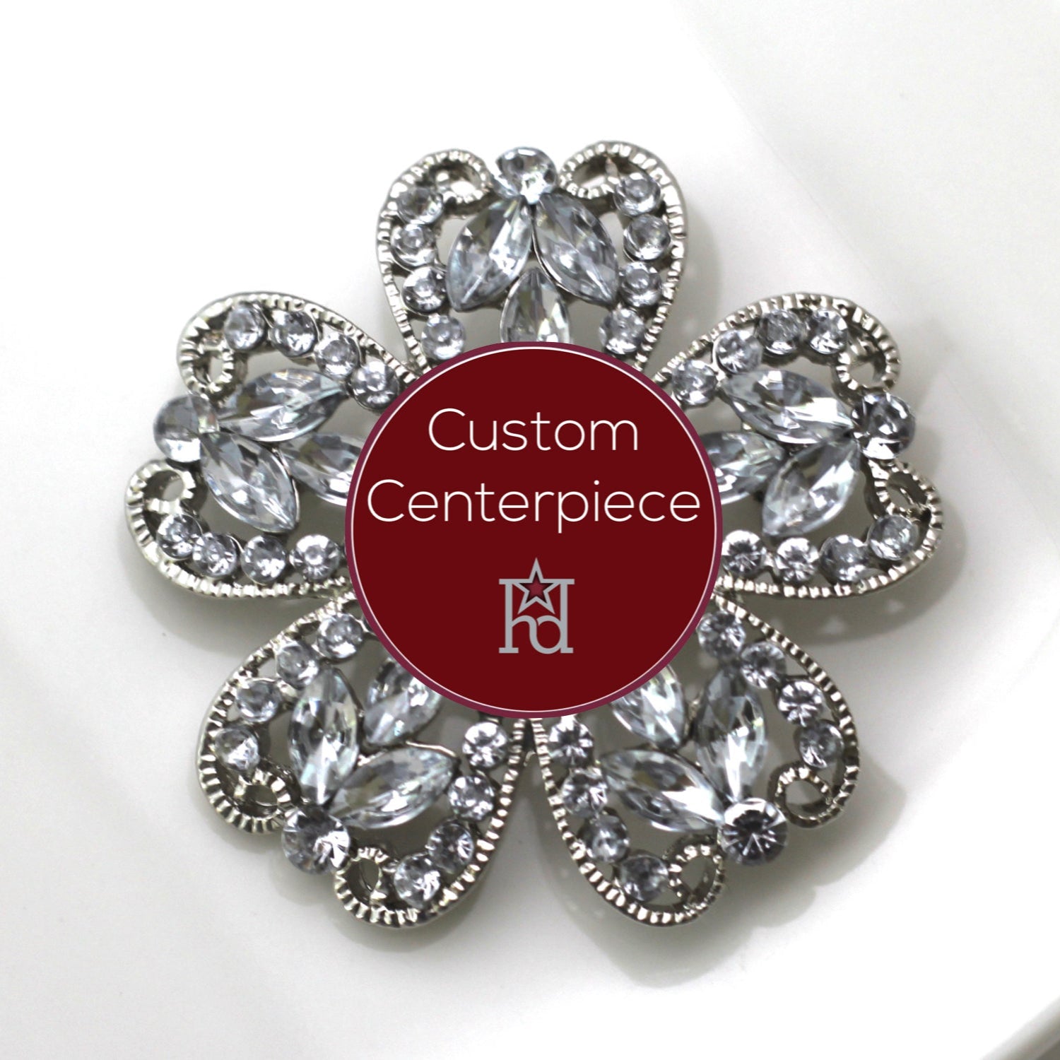 A silver brooch with clear crystal embellishments in a floral pattern with a central red label stating 'Custom Centerpiece'.