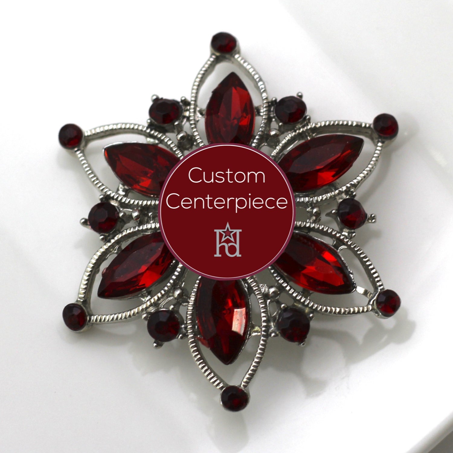 A silver brooch with red crystals designed as a custom centerpiece, displayed on a white plate.