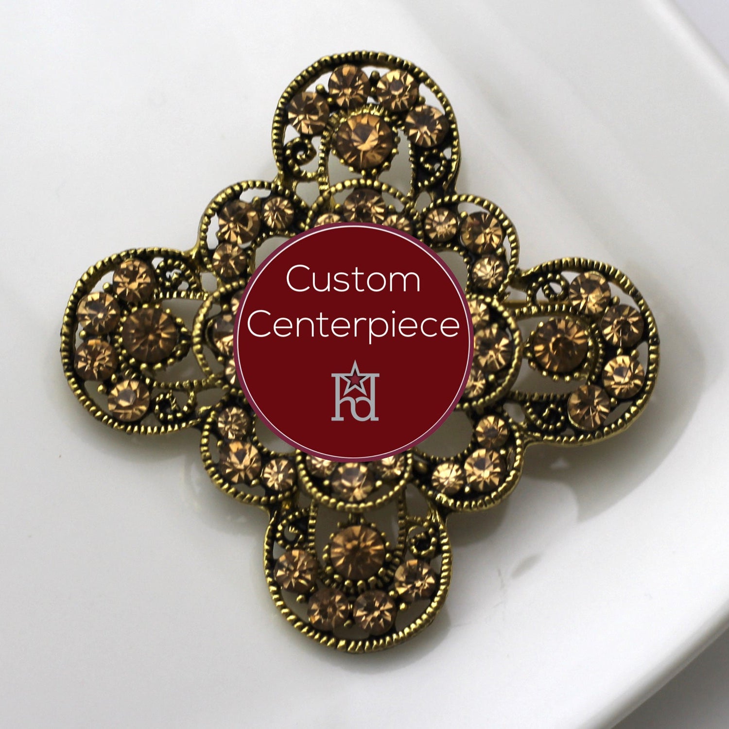 A gold-colored brooch with citrine crystals designed as a custom centerpiece, displayed on a white plate.