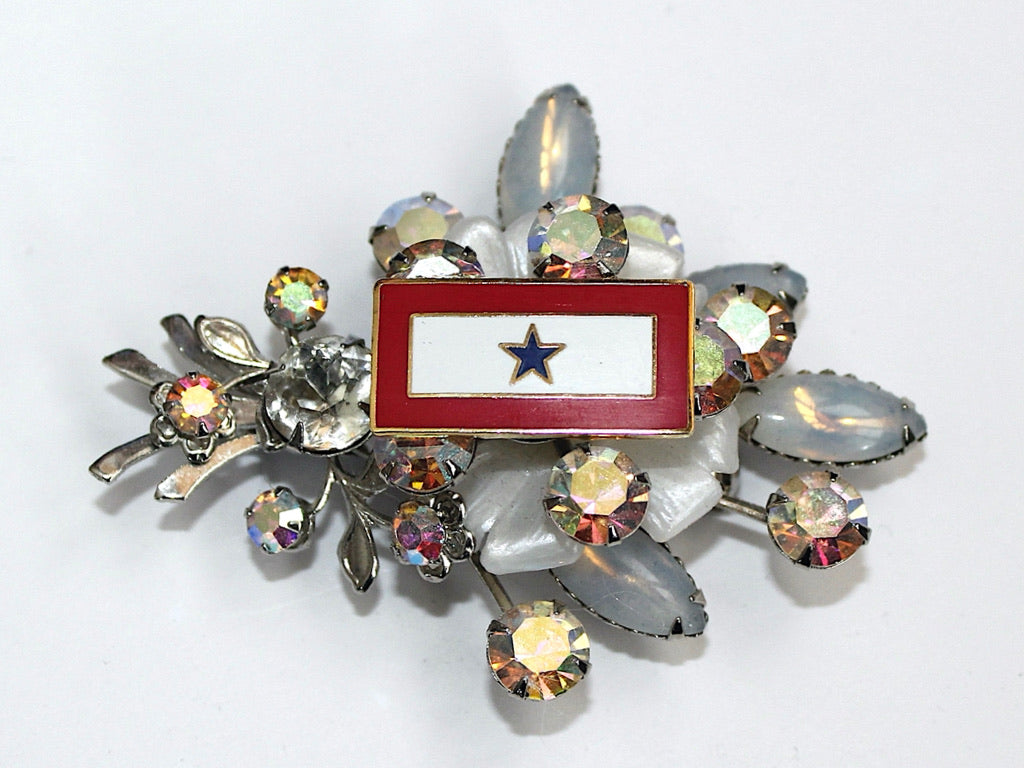 Vintage brooch with a blue star and red background, encircled by clear crystals and silver-colored metal accents.