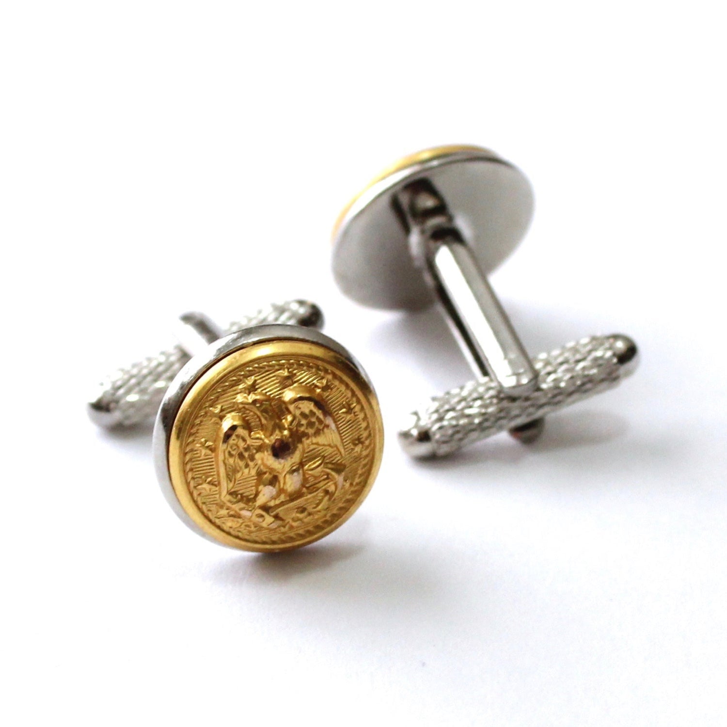 A pair of gold-tone button cufflinks with intricate button detailing, placed on a white background.
