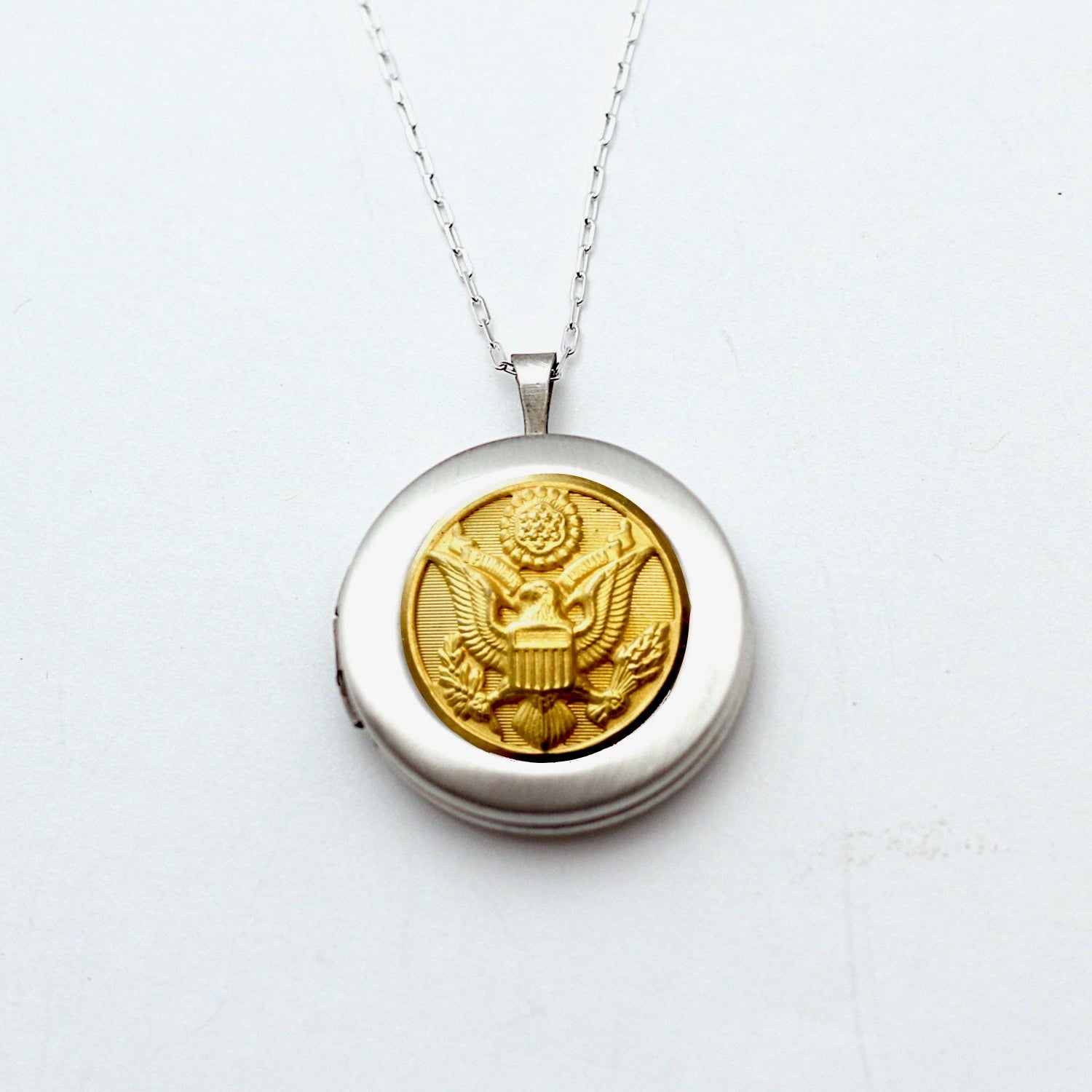 A silver locket necklace featuring a button design, with a silver chain and a lobster claw clasp, on a white background.