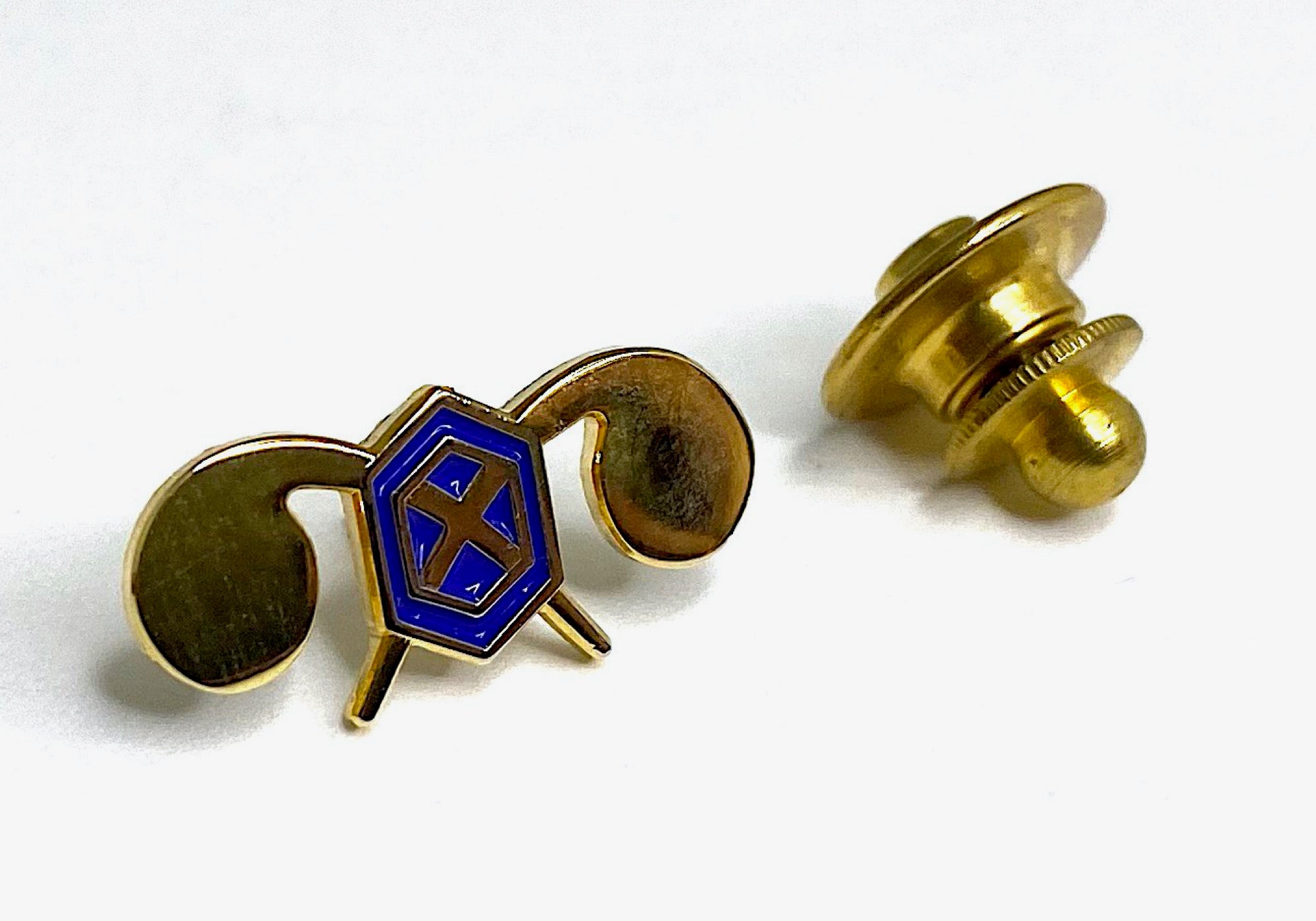 A gold-colored lapel pin with a blue, white, and gold geometric design and a clasp fastener.