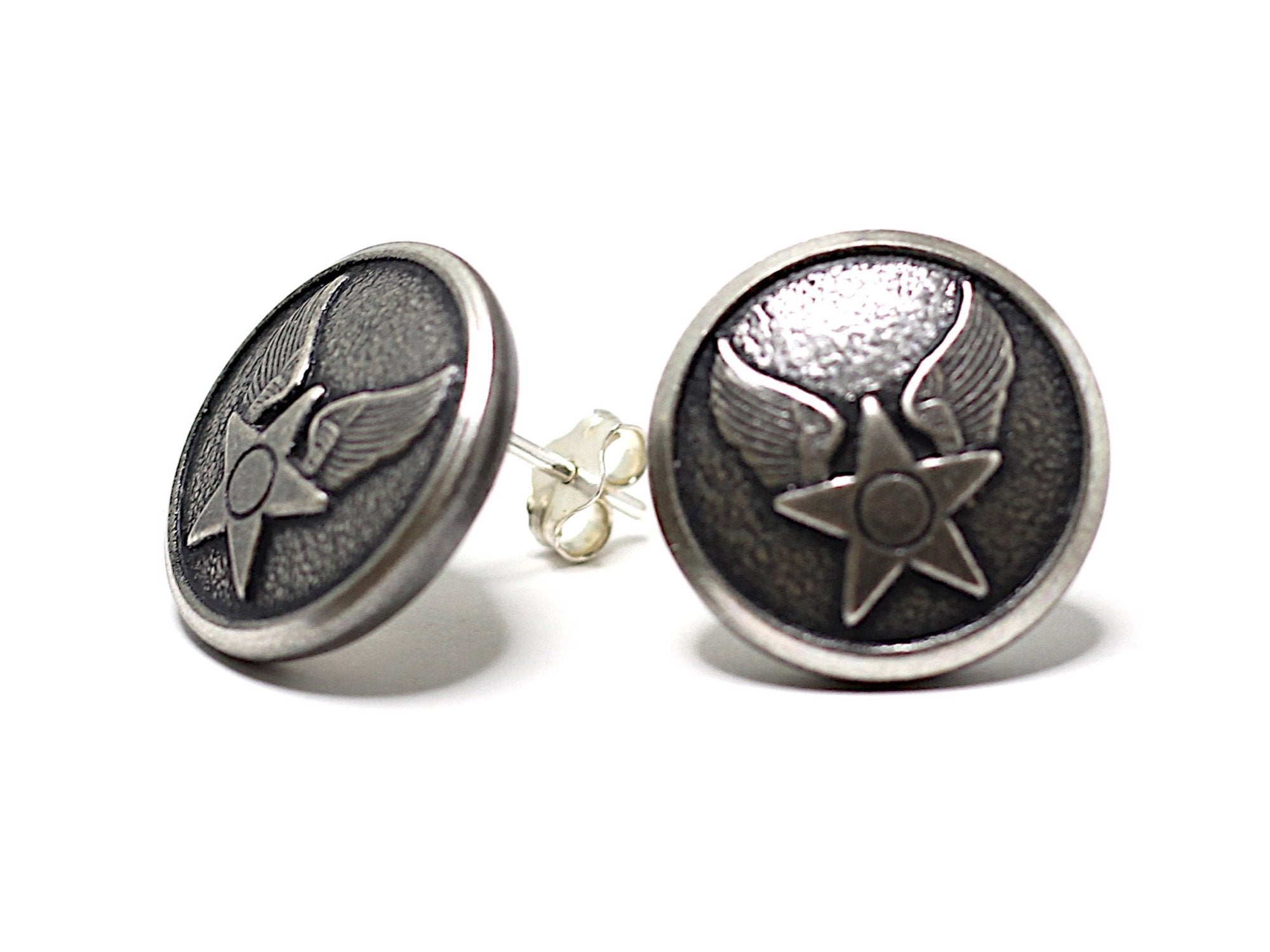 A pair of button post earrings with a star and wing design on a silver-colored surface.