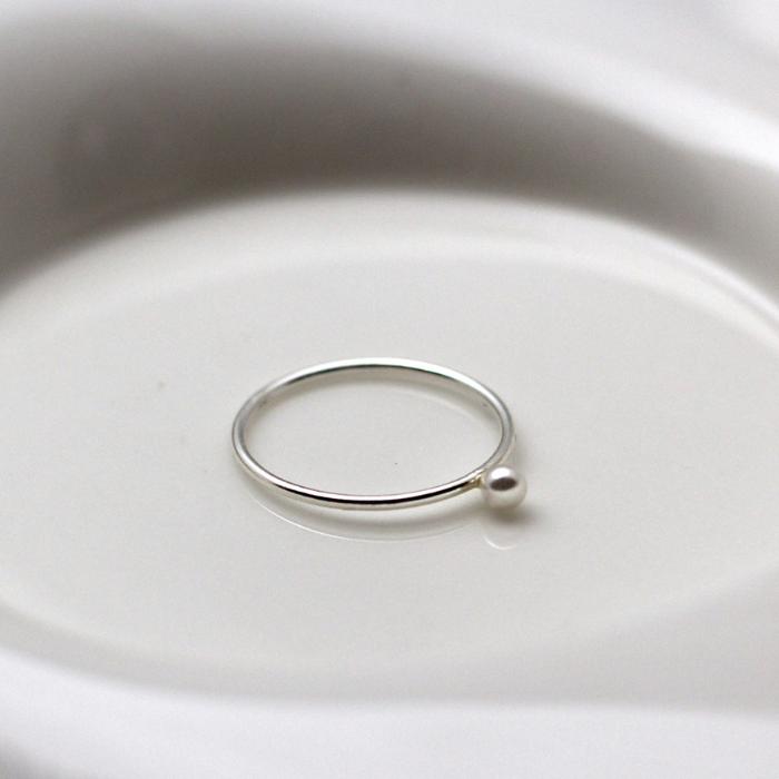 Silver ring with a small pearl on a white dish