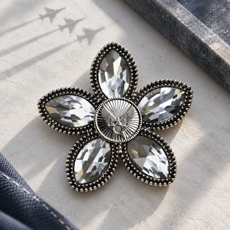 A flower-shaped brooch with clear crystal rhinestones and an antiqued silver-tone border, featuring an Air Force motif. The brooch is displayed on a textured light beige stone surface.