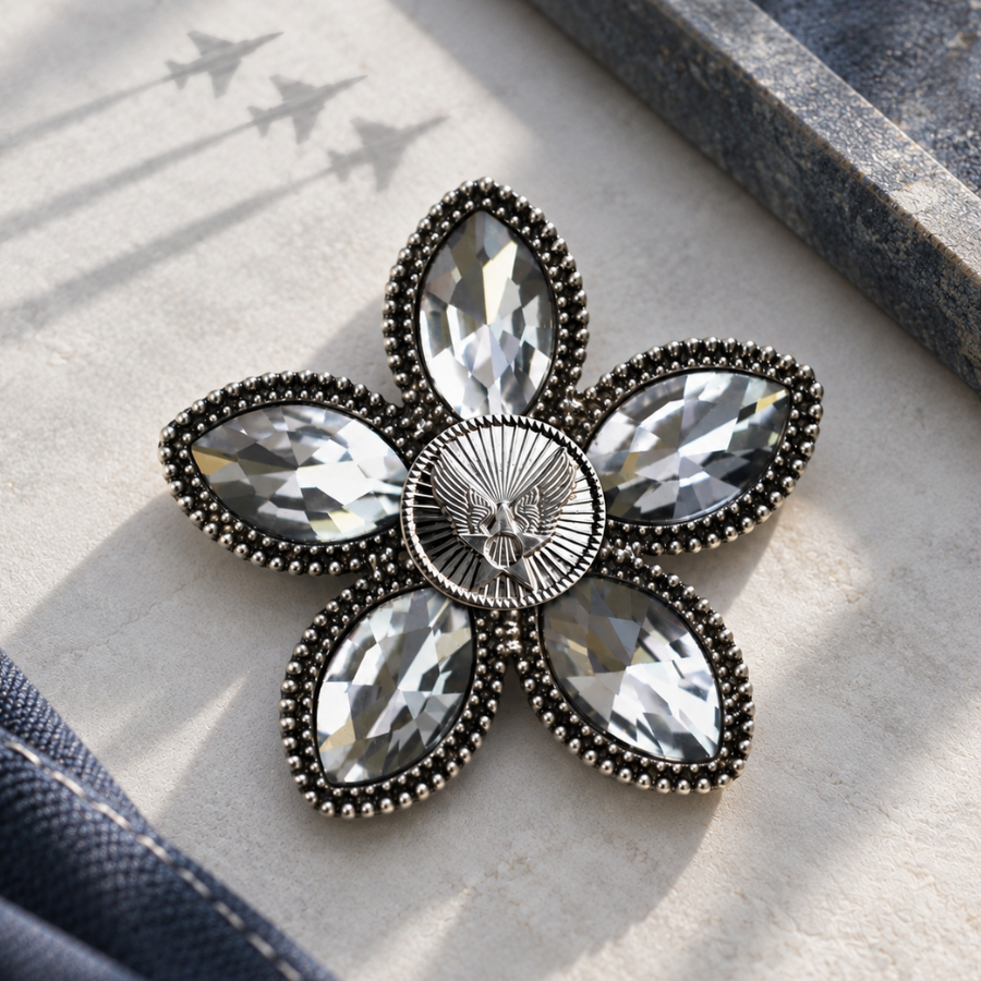 A flower-shaped brooch with clear crystal rhinestones and a silver-tone metal border, featuring a air force motif. The brooch is displayed on a textured light beige stone.