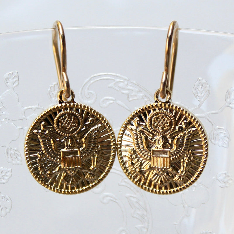 Army inspired gold french wire earrings on a glass and white background