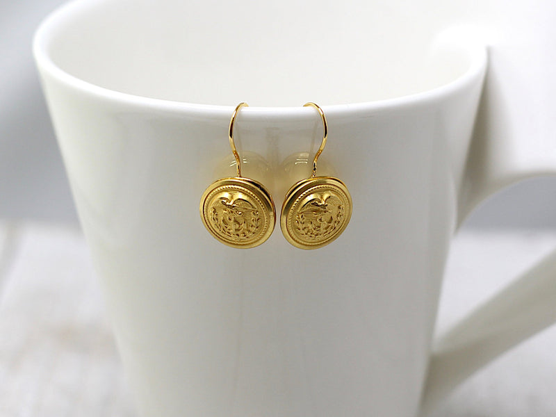 Gold Coast Guard button french wire earrings on a white cup