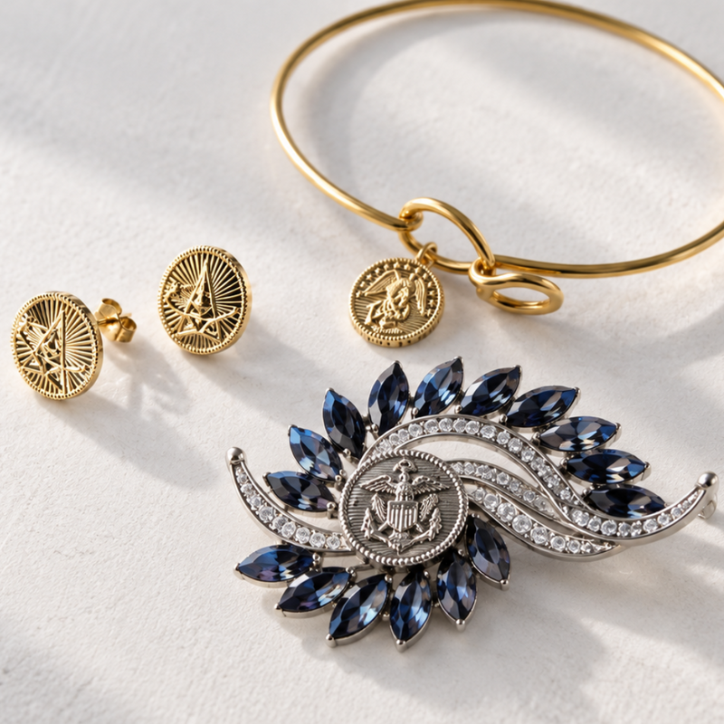 A gold bangle bracelet with a circular medallion charm, a pair of matching gold stud earrings, and a silver and blue gemstone sunburst brooch, all arranged on a white textured surface with soft diagonal shadows.