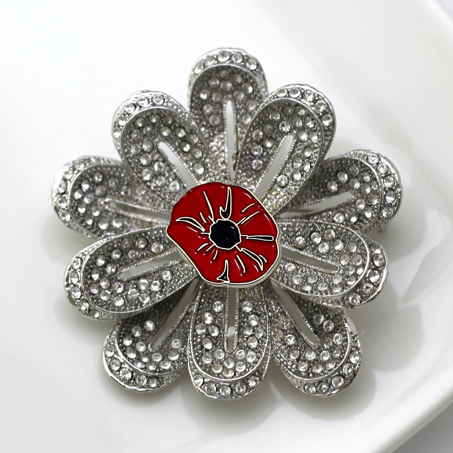 Silver flower-shaped brooch with a red center on a white background