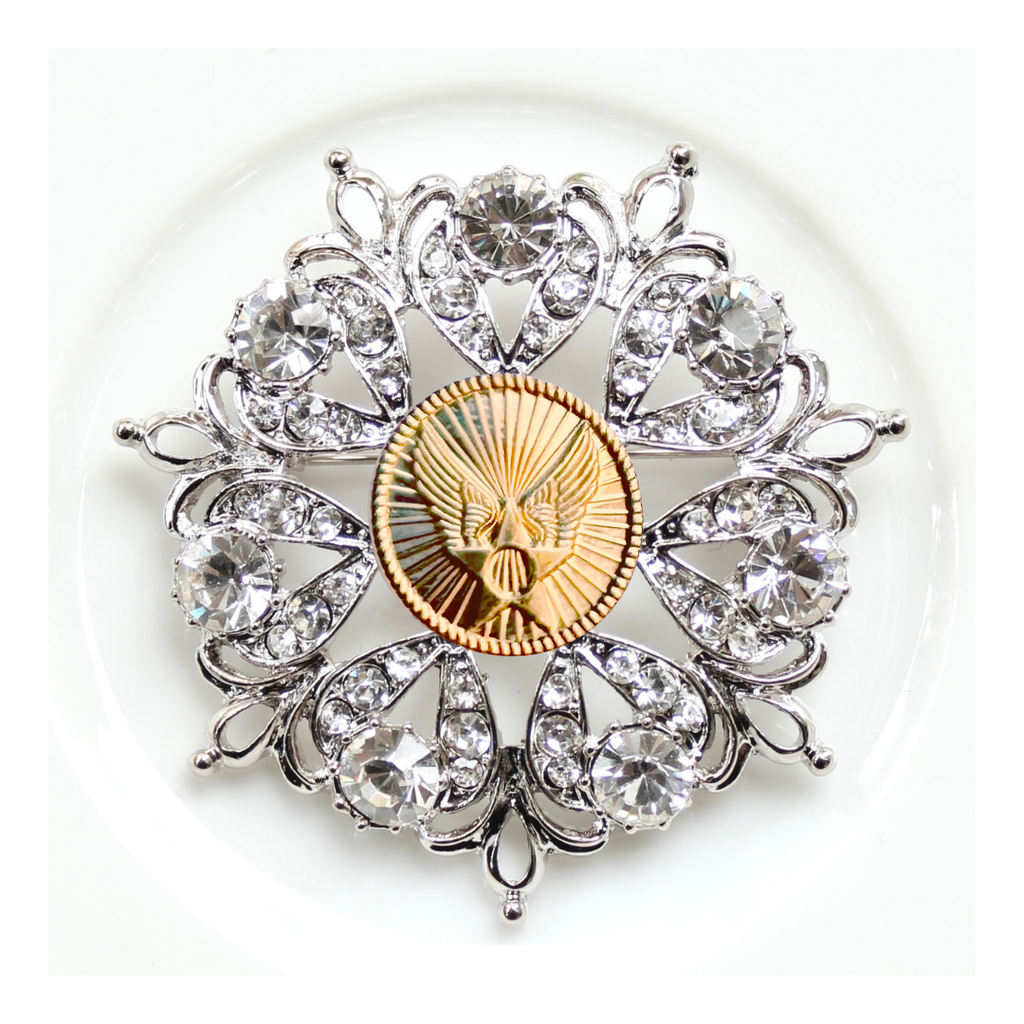 Decorative brooch with crystal elements and a gold center on a white background