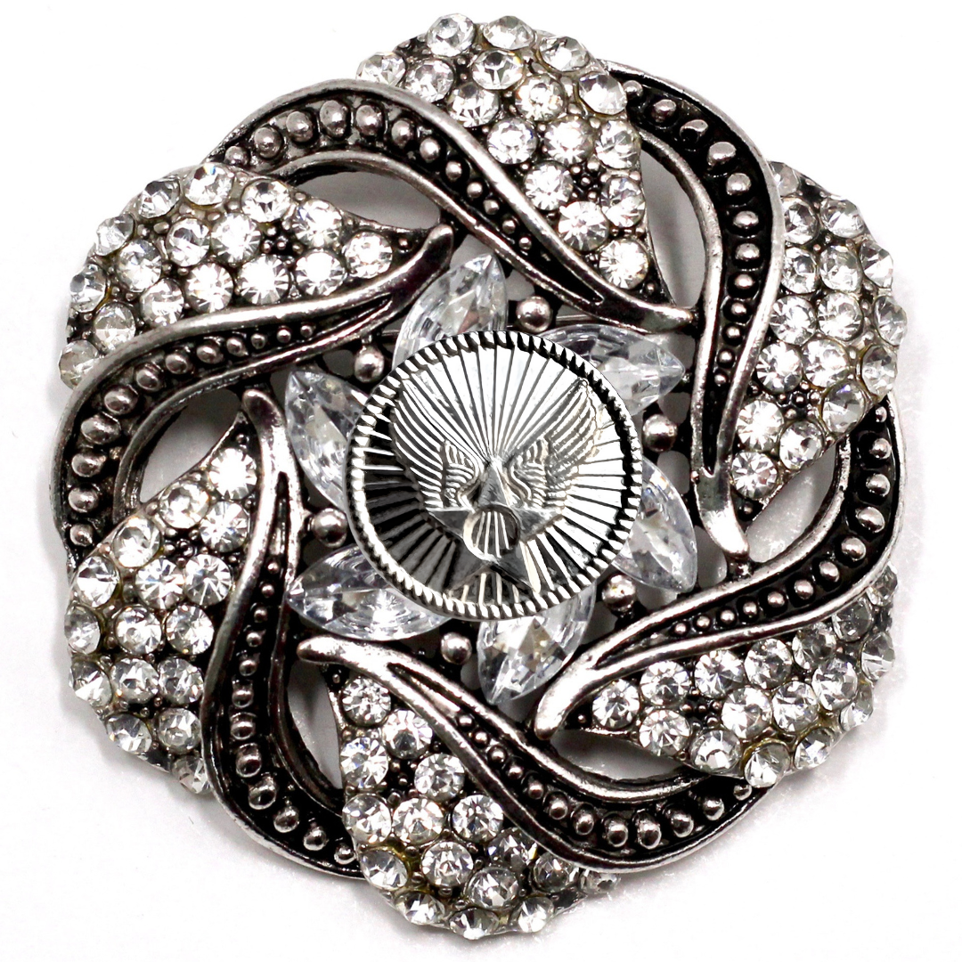 Decorative brooch with intricate design and sparkling stones on a white background