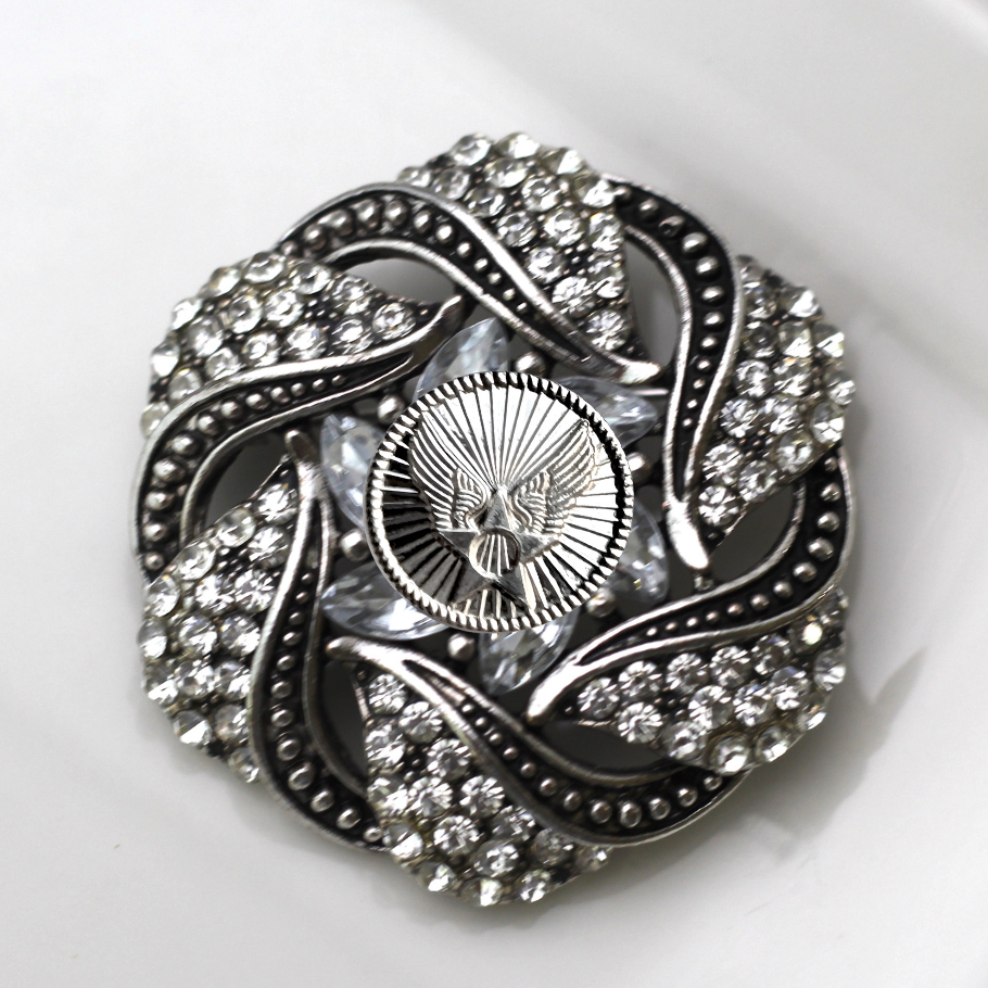 Decorative brooch with intricate design and sparkling stones on a white background