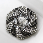 Decorative brooch with intricate design and sparkling stones on a white background
