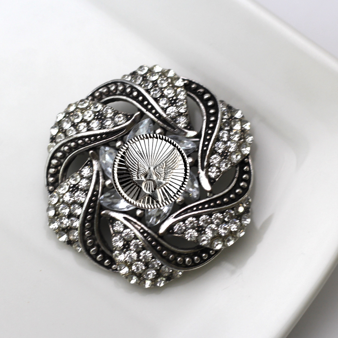 Decorative brooch with intricate design and sparkling stones on a white background