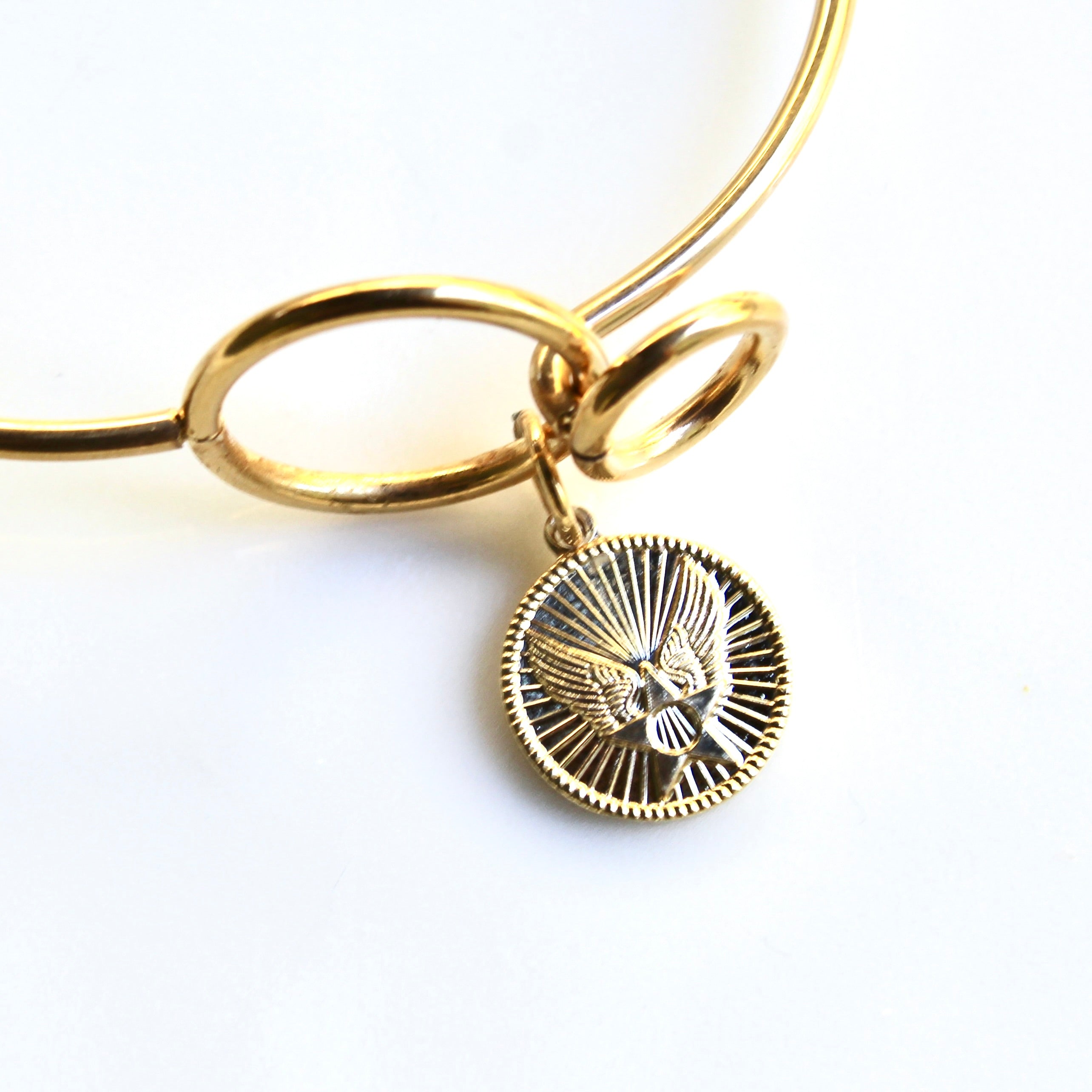 Gold bracelet with a circular charm on a white background