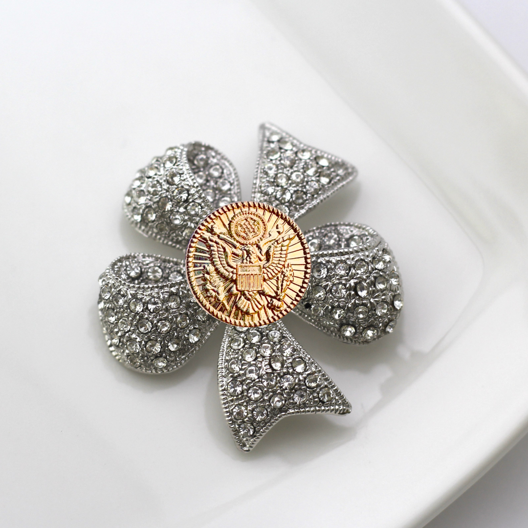 Decorative brooch with central emblem and surrounding crystals on a white background