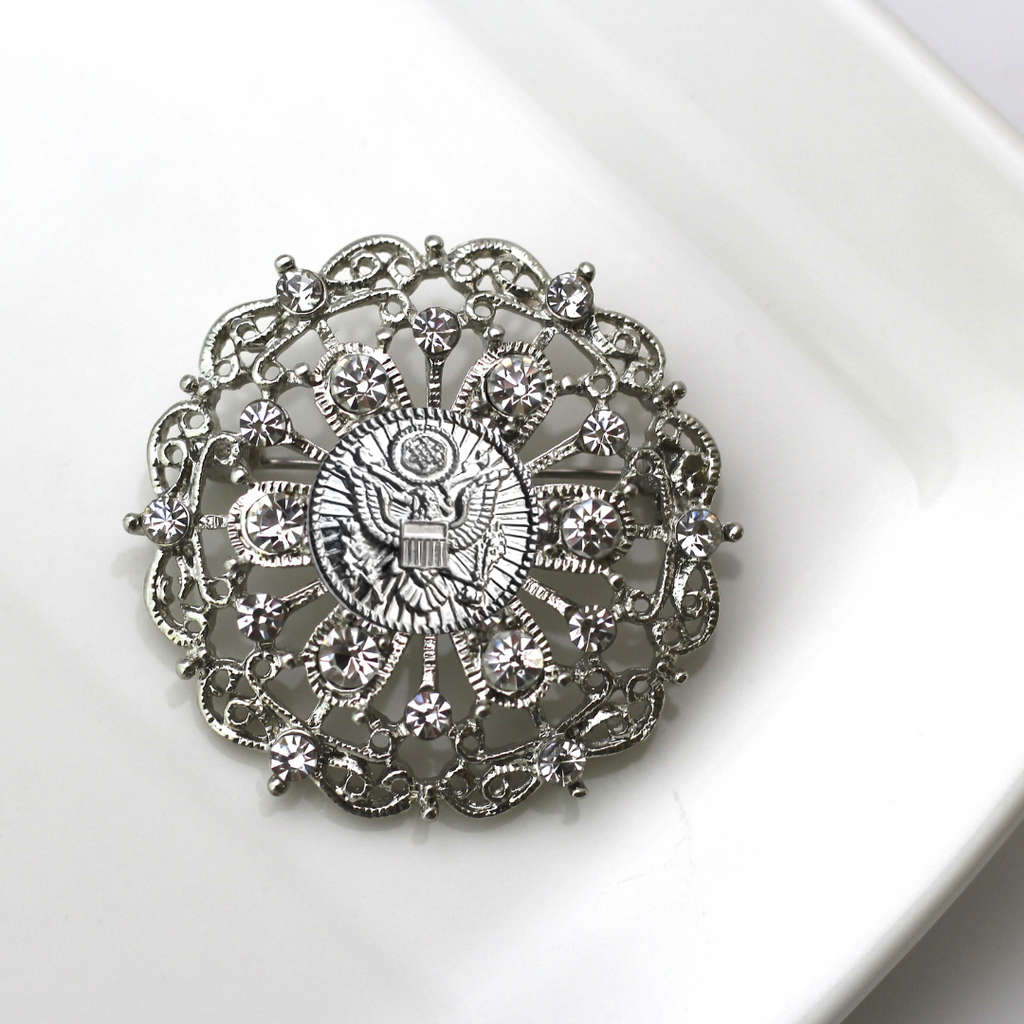 Decorative brooch with intricate design and central Army inspired emblem on a white background