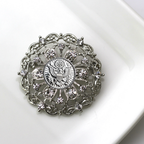 Decorative brooch with intricate design and central Army inspired emblem on a white background