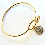 Gold bangle with a tree of life charm on a white background