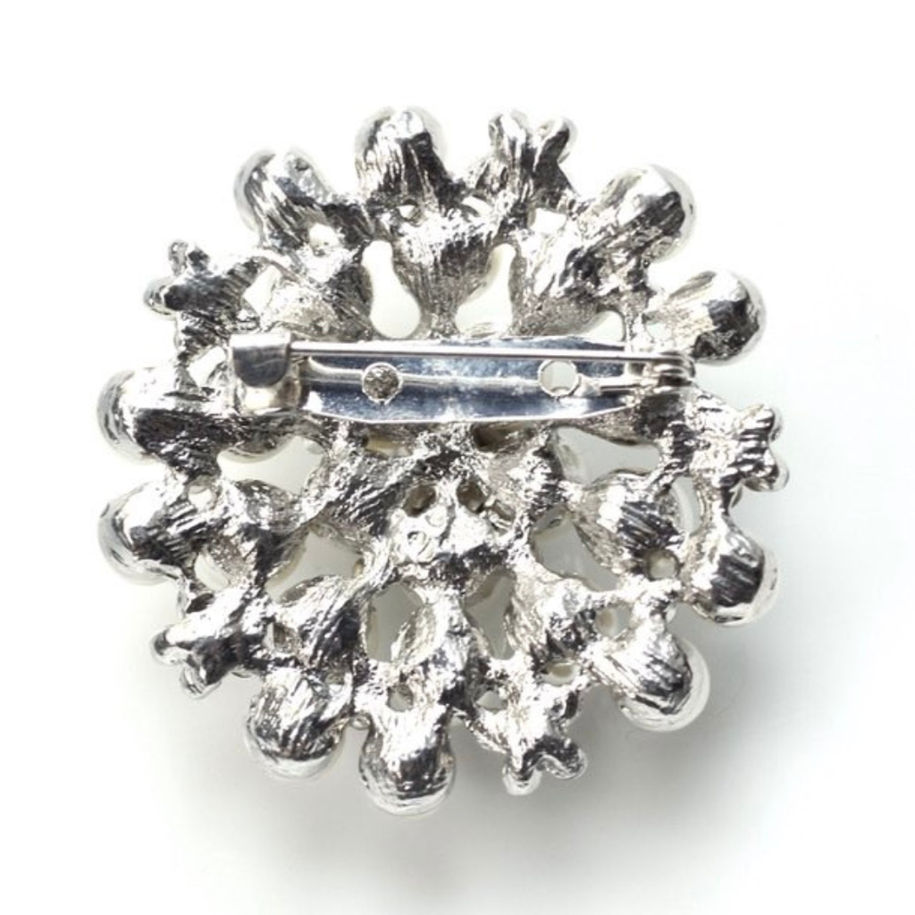 Silver brooch with intricate design on a white background