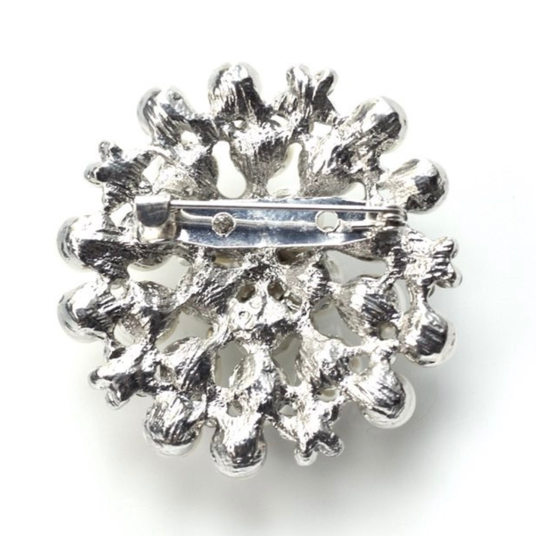 Silver brooch with intricate design on a white background