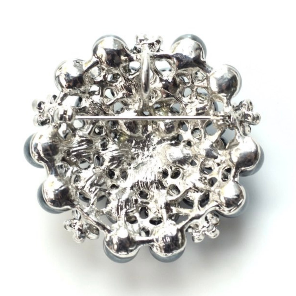 Silver brooch with intricate design on a white background