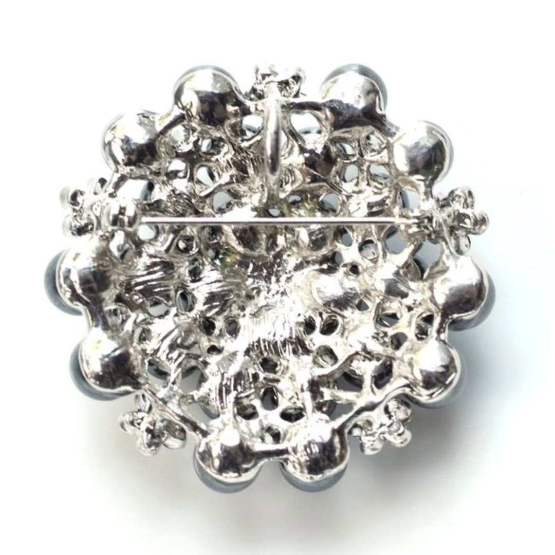 Silver brooch with intricate design on a white background