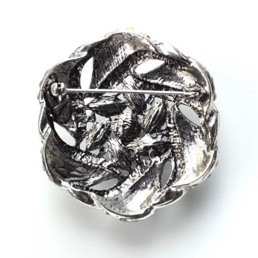 Silver brooch with intricate design on a white background