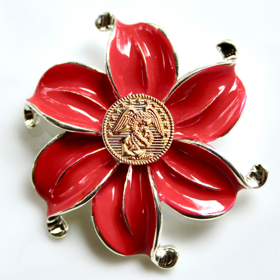Red flower-shaped brooch with gold center on a white background