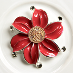 Red flower-shaped brooch with gold center on a white background