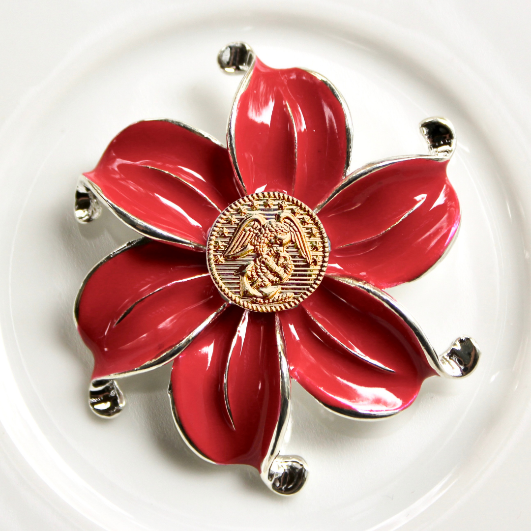 Red flower-shaped brooch with gold center on a white background