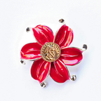 Red flower-shaped brooch with a gold center on a white background