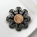 Decorative brooch with black gemstones and gold Marines inspired center on a white background