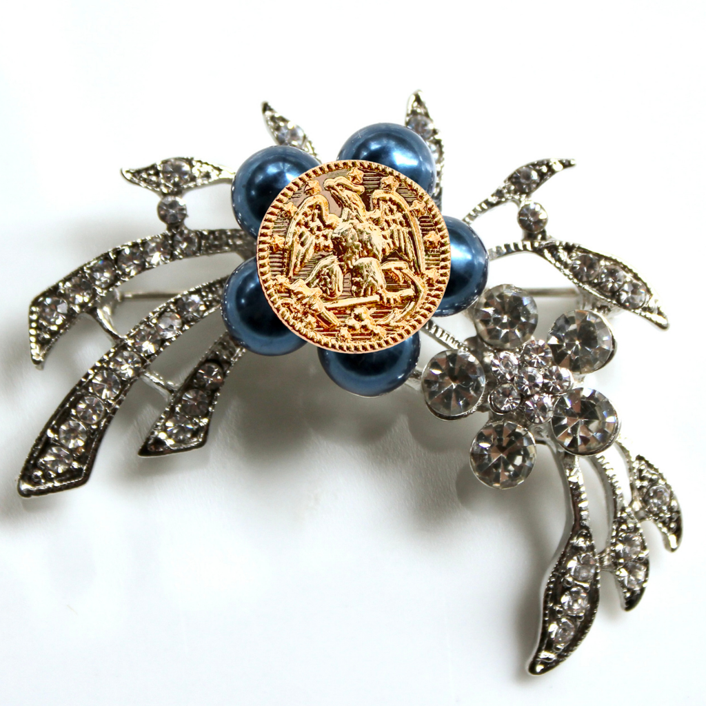 Decorative brooch with blue pearls, gold emblem, and silver leaves on a white background
