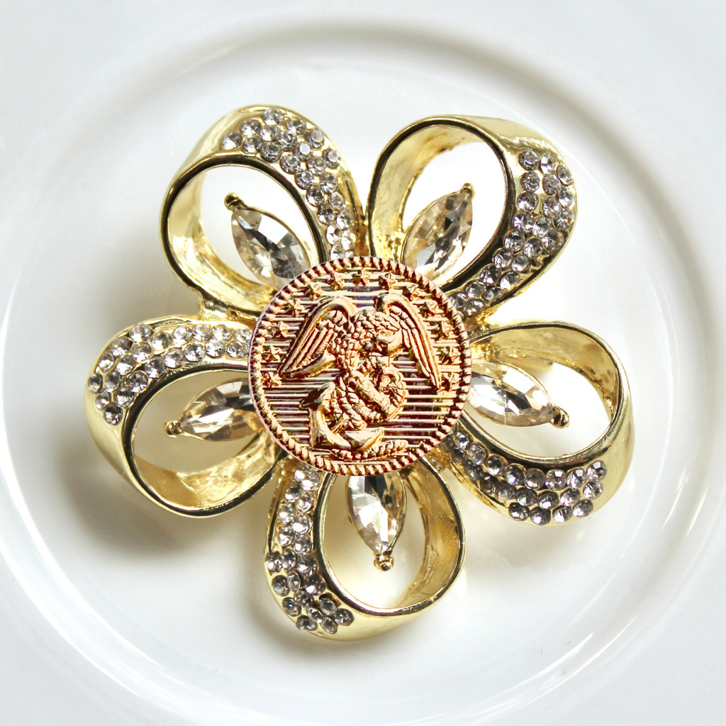 Gold brooch with floral design and central emblem on a white background