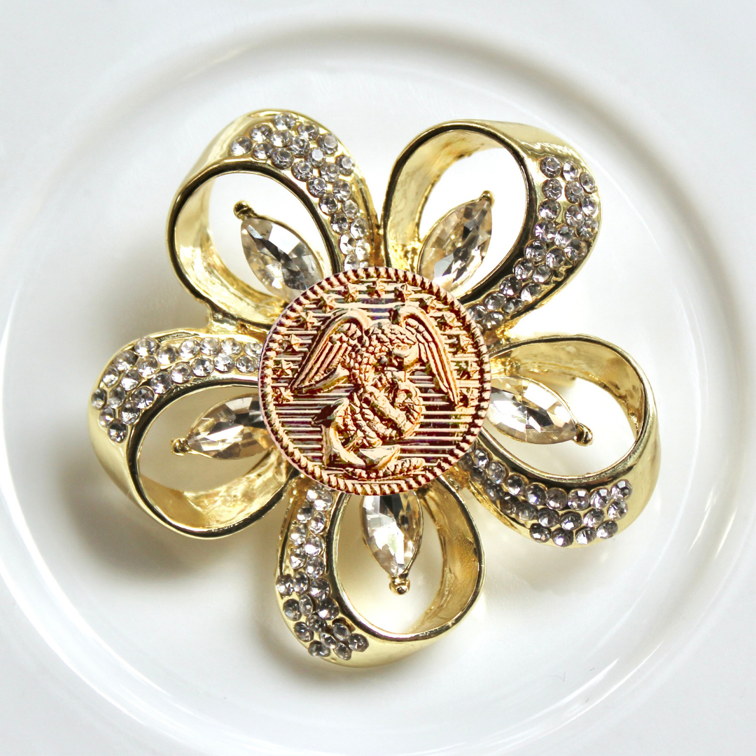 Gold brooch with floral design and central emblem on a white background