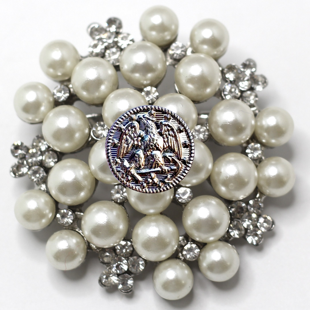 Brooch with pearls and a central emblem on a white background