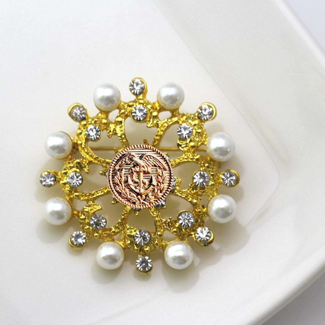 Decorative brooch with gold elements, pearls, and a Coast Guard emblem on a white background