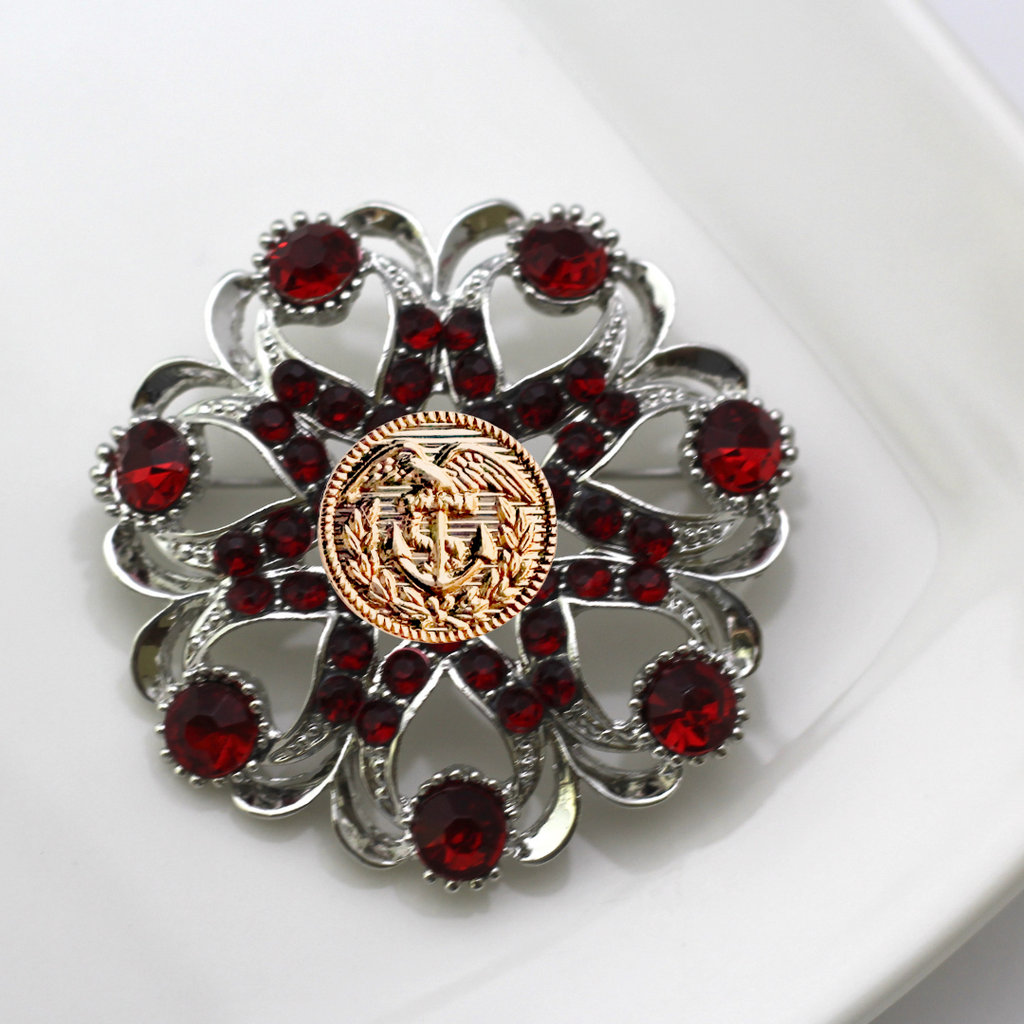 Decorative brooch with red gemstones and a gold Coast Guard center on a white background