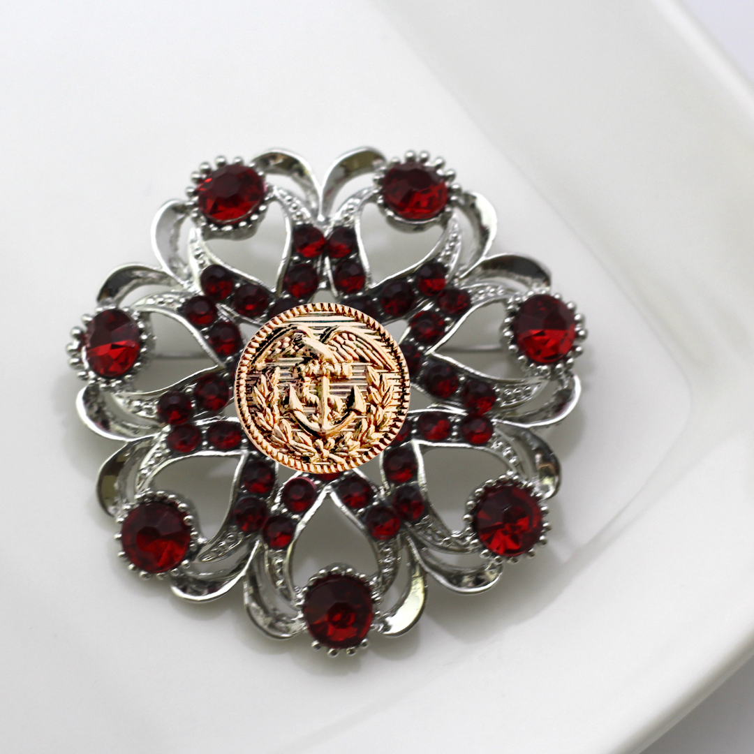 Decorative brooch with red gemstones and a gold Coast Guard center on a white background