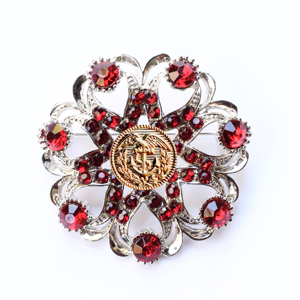 Decorative brooch with red gemstones and a gold Coast Guard center on a white background
